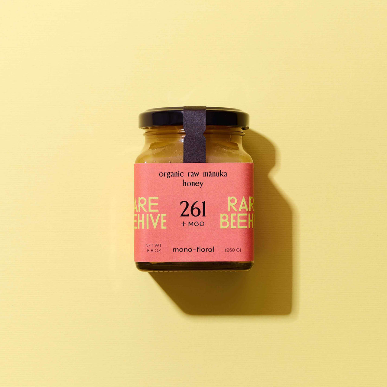 Jar of organic raw Mānuka honey with a pink label on yellow background